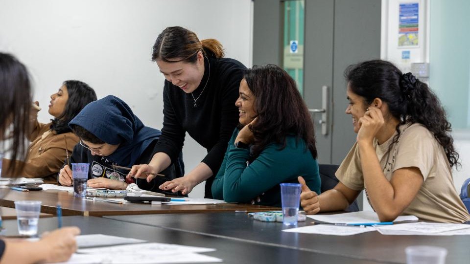 International students of different nationalities sat around tables painting with a student helping to teach them