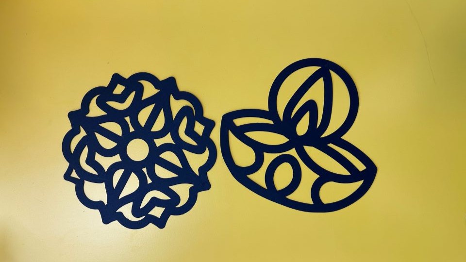 Two black cut out templates of Diwali inspired images - a diwa and a rangoli pattern - on a bright yellow background
