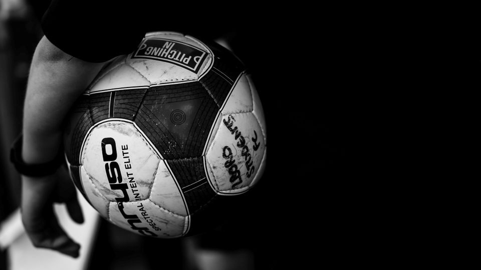 Black and white photograph of a football being held tucked under someone's arm.