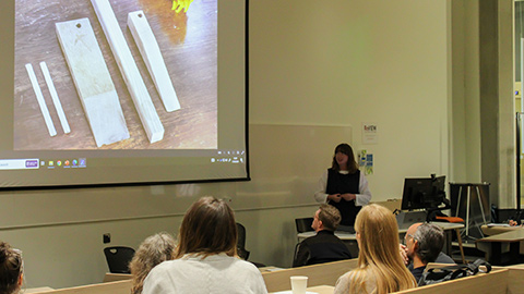 Harriet Morley standing by a computer and desk by a large screen talking about her project to a lecture theatre of people