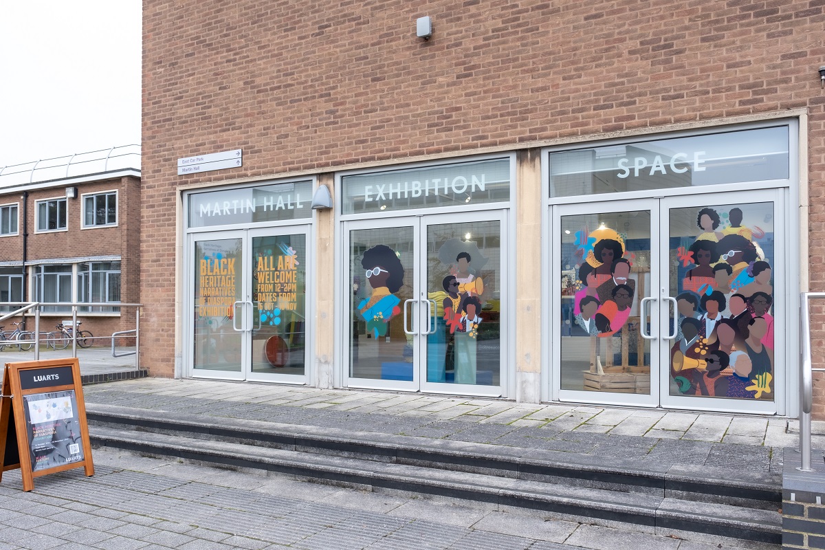 The outside of Martin Hall Gallery with all 6 windows featuring a colorful illustrated mural with black caricatures by Candis Boateng