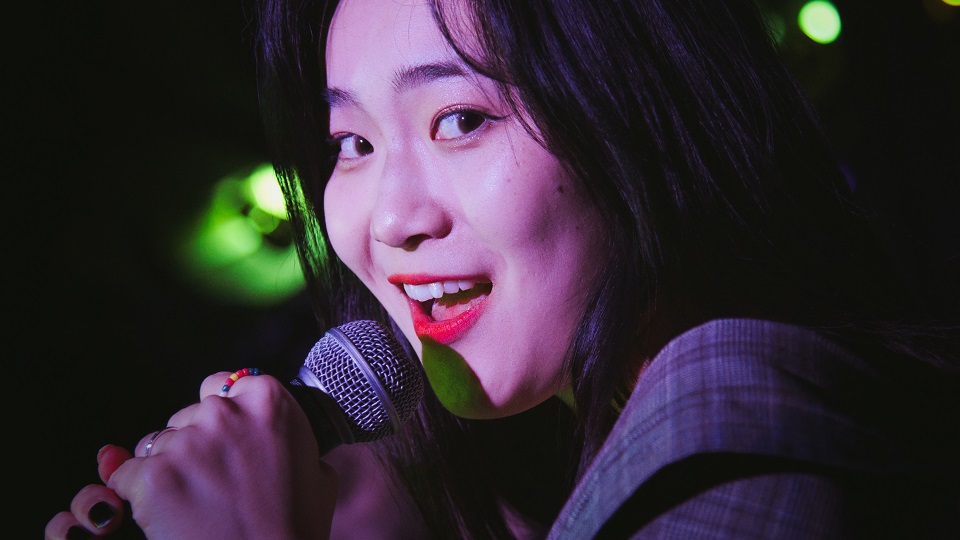 A young student of East-asian decent singing and smiling into a microphone