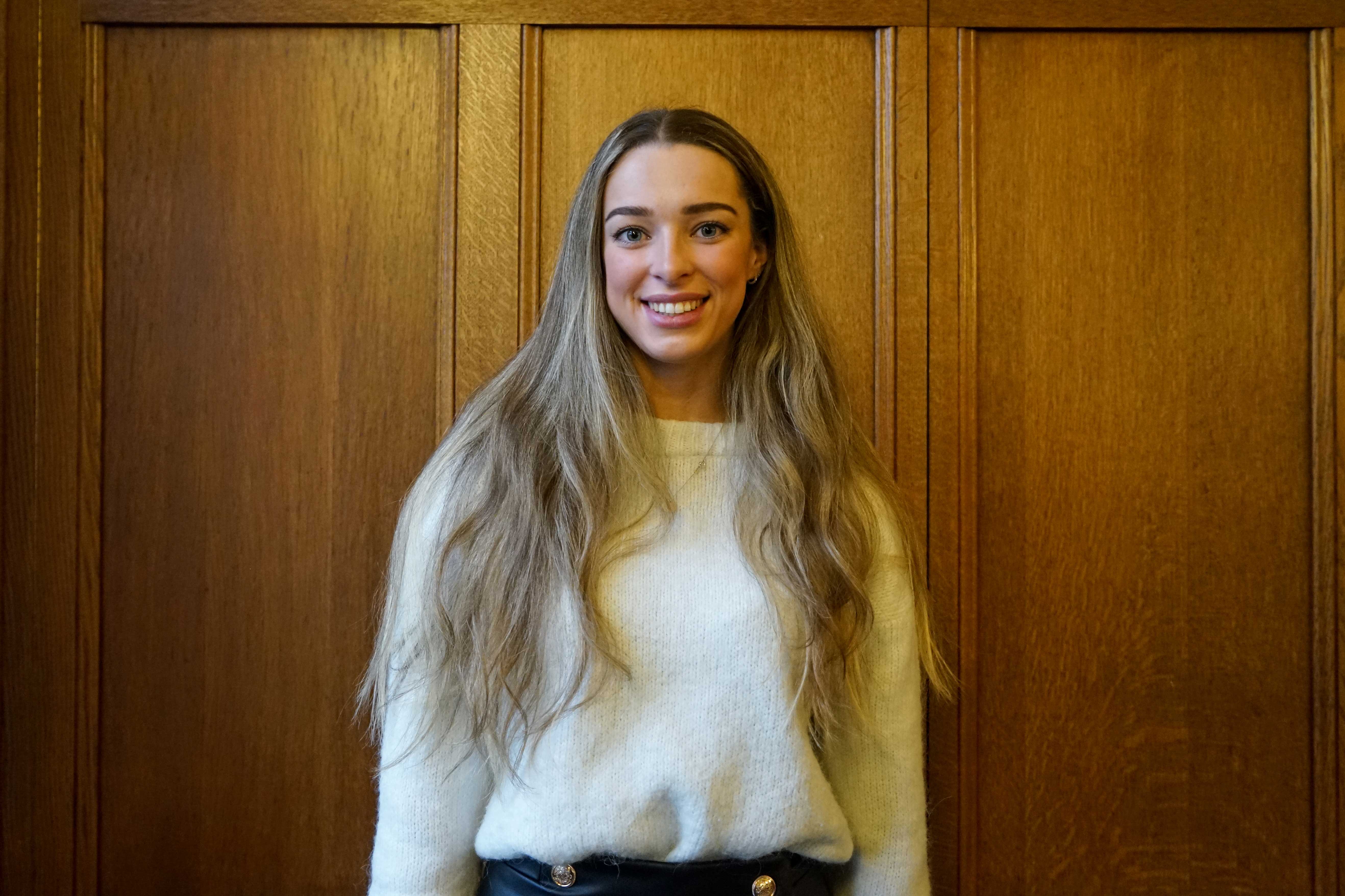 A white female student in her early twenties smiling at the camera. She is wearing a cream jumper and has very long straight blonde hair. 