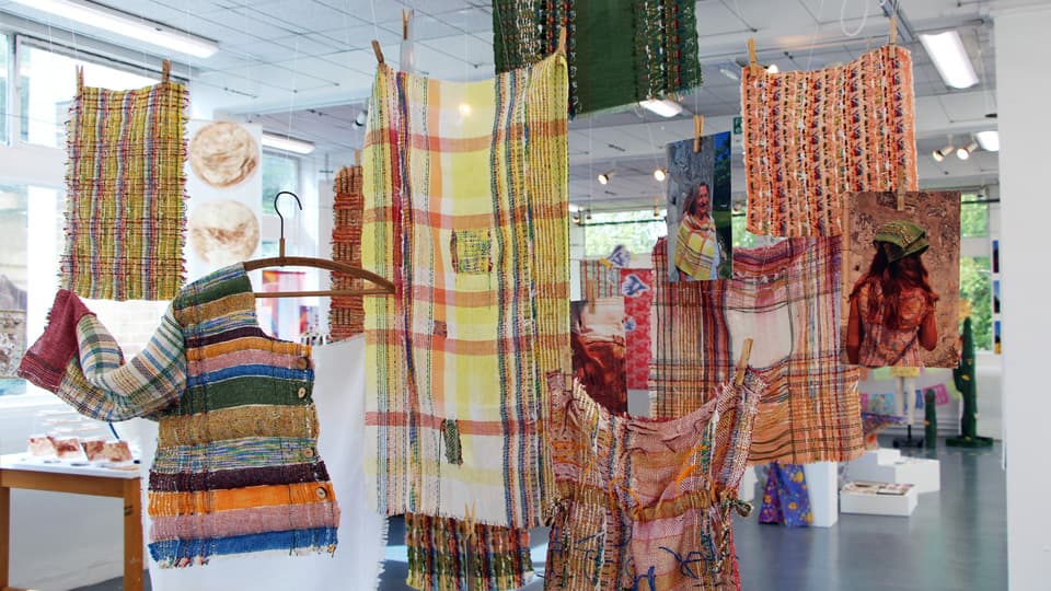 Abstract textile artwork in shades of orange and yellow, hanging from the ceiling.