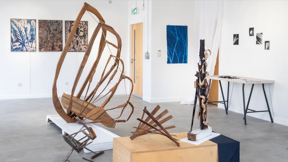 An abstract wooden sculpture in a white exhibition space.