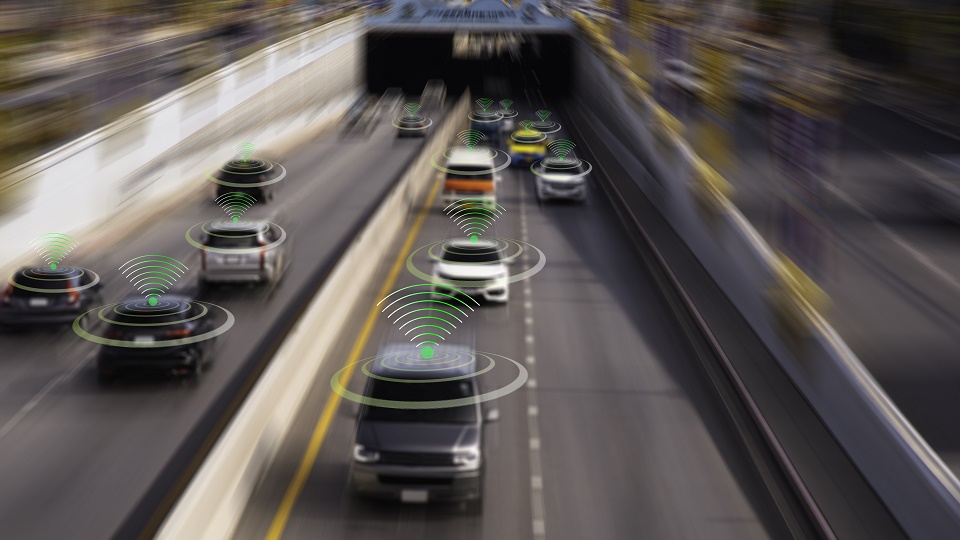 Cars travelling along a road with graphics above them to signify autonomous vehicles.
