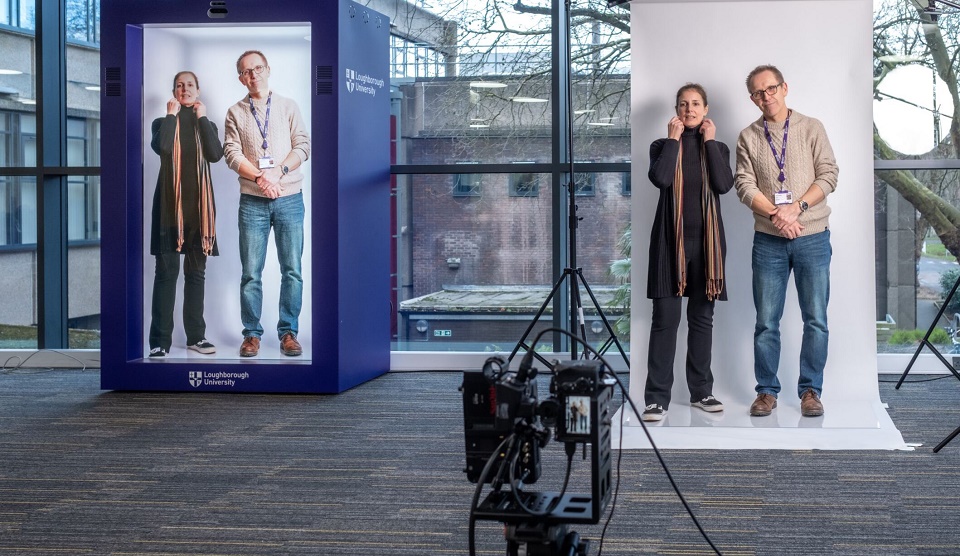 A woman and a man try out new hologram technology, being filmed on a camera and then appearing on the hologram screen next to them.