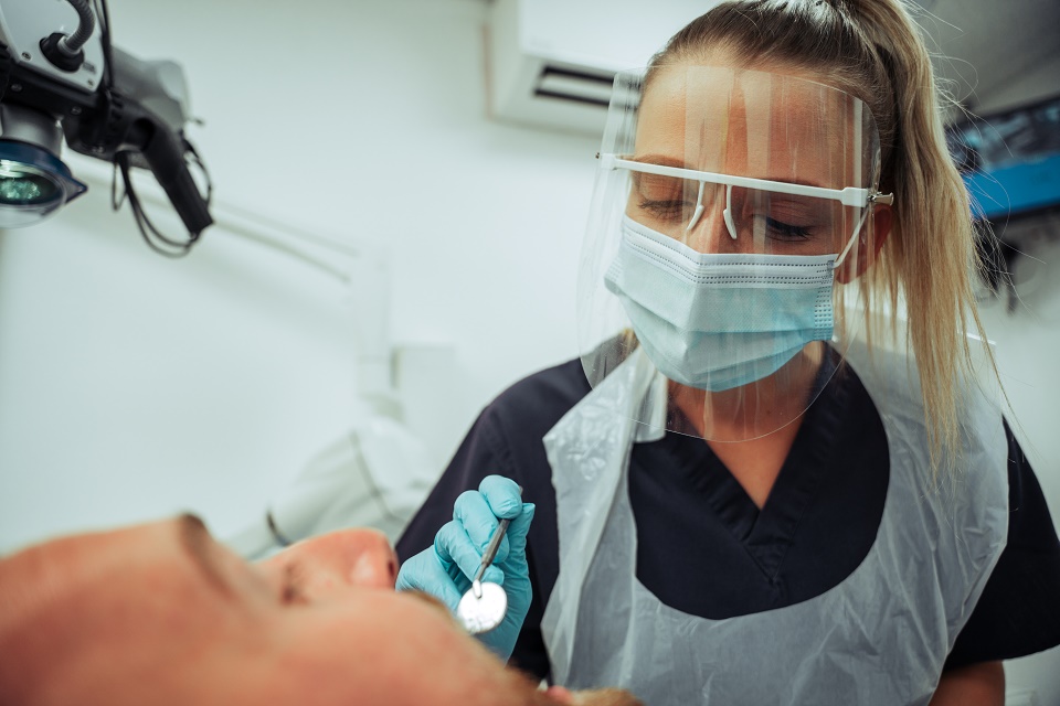 A female dentist is examining a male patient's teeth