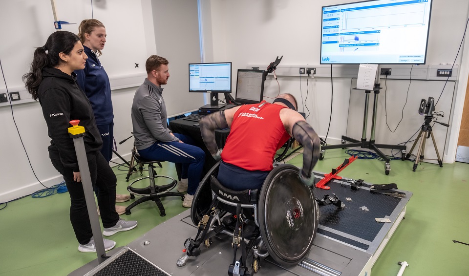 A para athlete in a wheelchair undergoes some testing with three researchers.