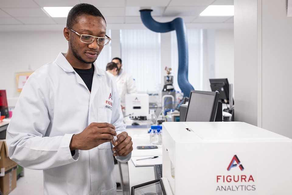 A man, wearing a white lab coat, analyses a liquid sample using specialist equipment