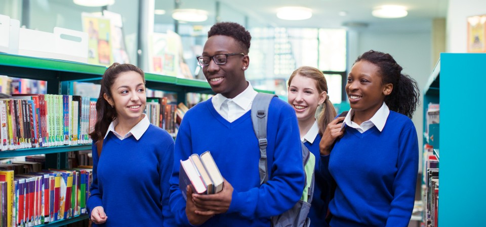 A school boy and three school girls laugh and walk together