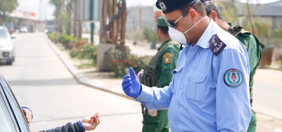 A Palestinian man in a face mask speaks to a person in a car