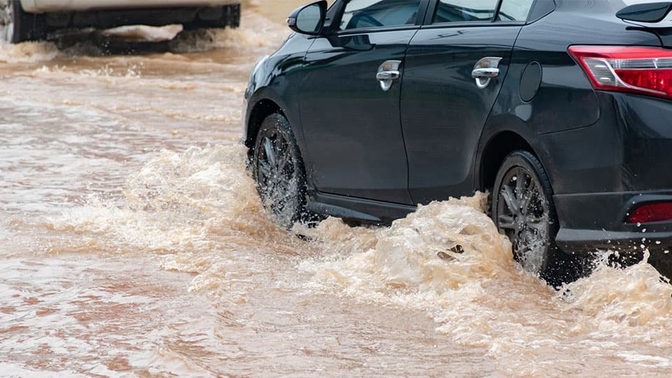A black car driving through muddy flood water