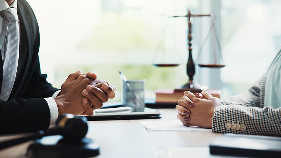Two sets of hands clasped over a table with a legal symbol in the background