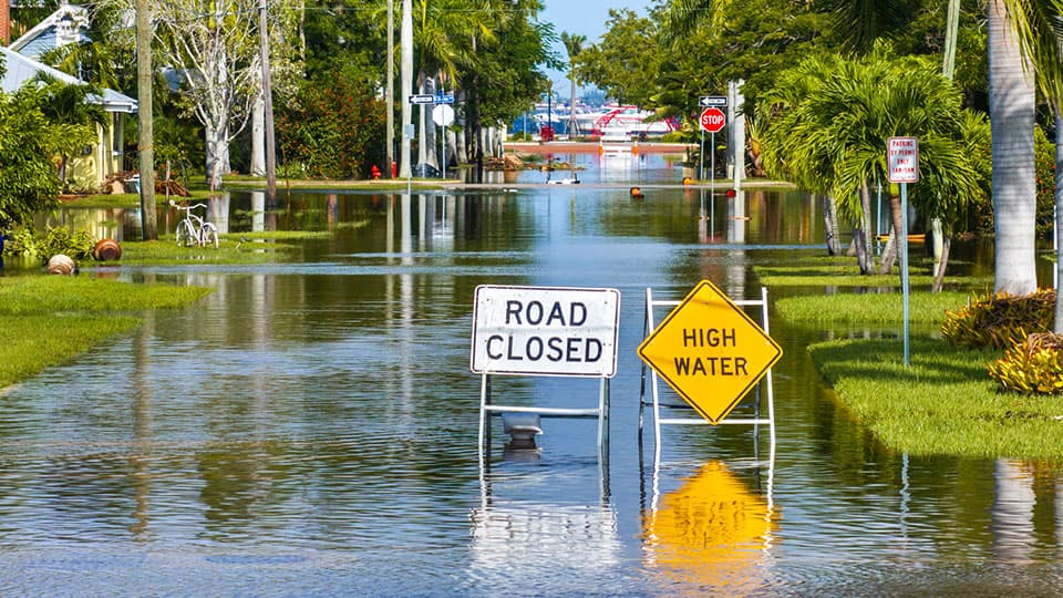 A flooded road with a closed road sign and high water sign