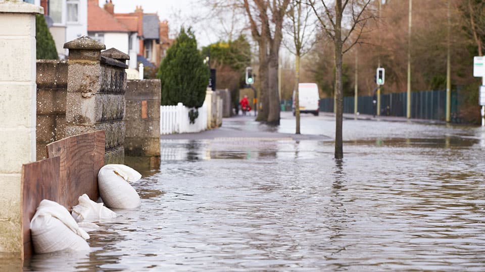 Sandbags propped up against a home on a flooded road