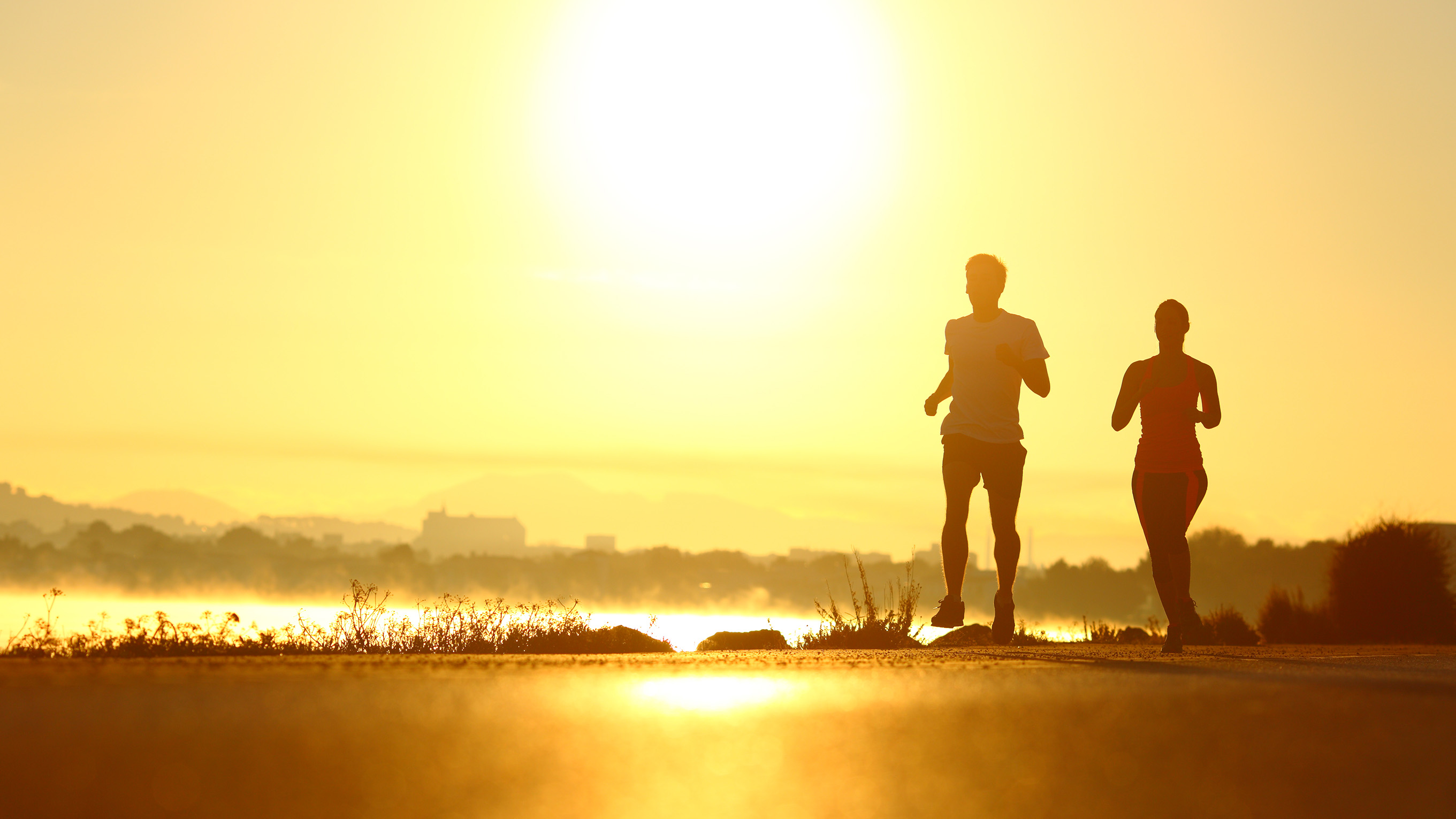 Two runners running along coastline in sunshine