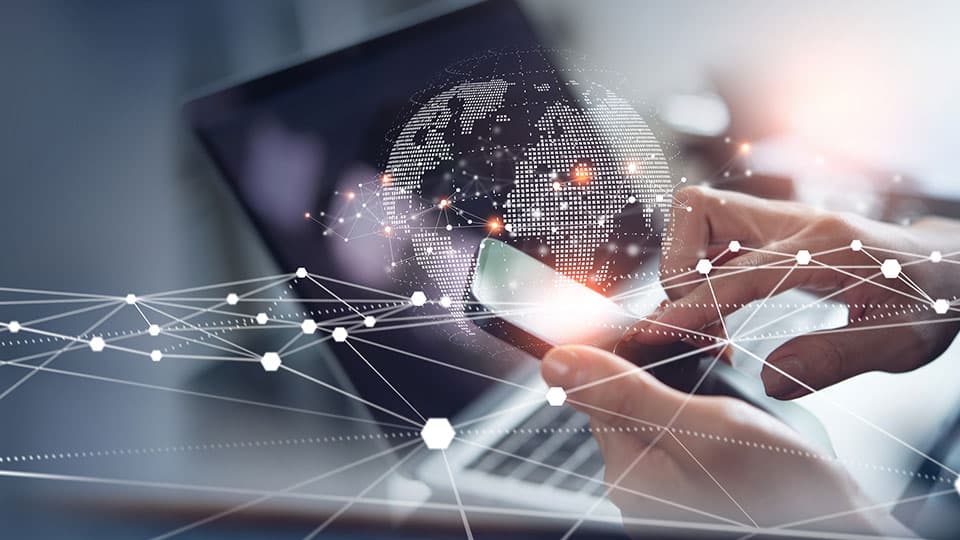 A person using a laptop and phone with graphics of a globe in front