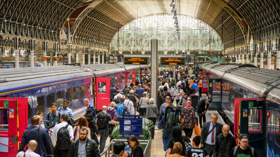 An indoor trains station with two train carriages in shot. There is a large group of people on the platform moving towards the carriages.