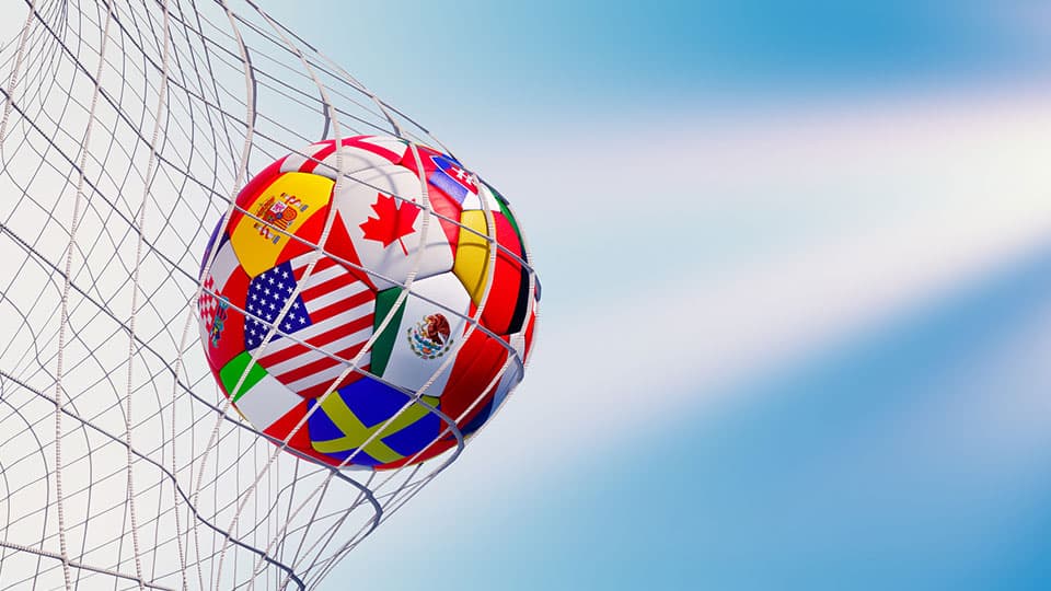 A football made from the flags of countries around the world being kicked into the back of the net