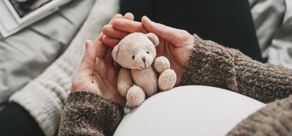 A pregnant woman holds a small teddy next to her belly