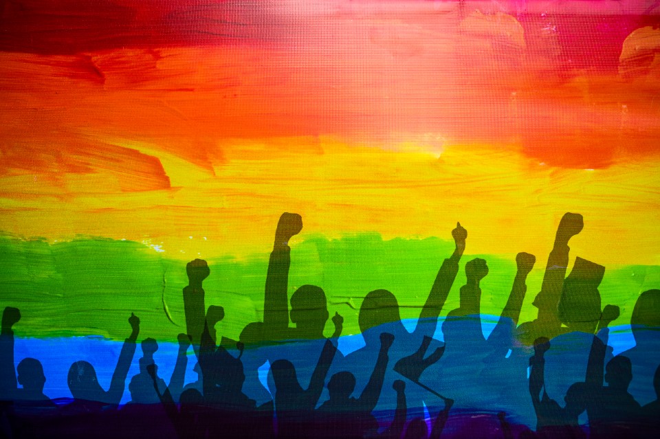 artwork showing a silhouette of a crowd with raised hands and a rainbow background