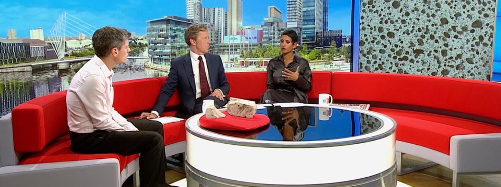 Three people sitting on a semi-circular sofa in a television studio