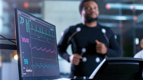 Athlete running on a treadmill next to a monitor with EKG data.