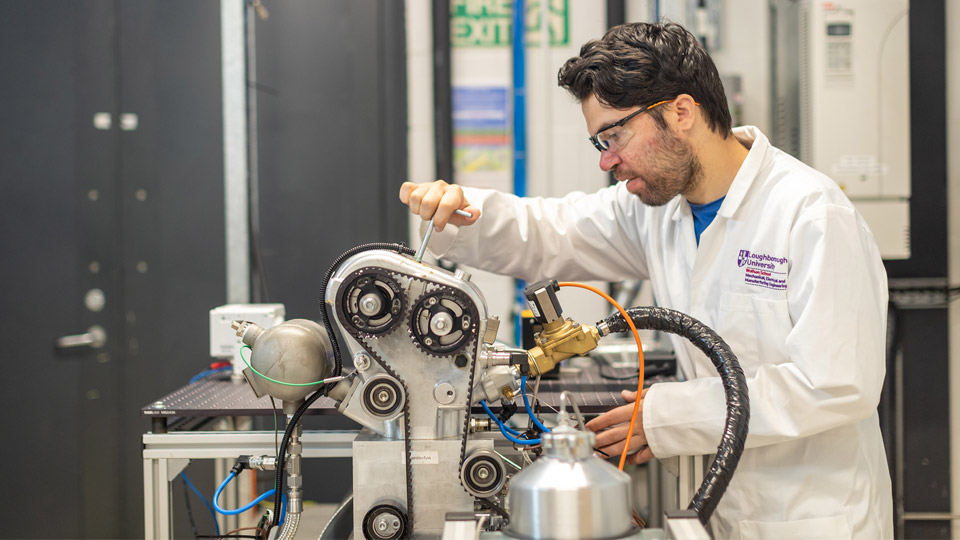 An engineer working in a lab wearing a lab coat and protective glasses.