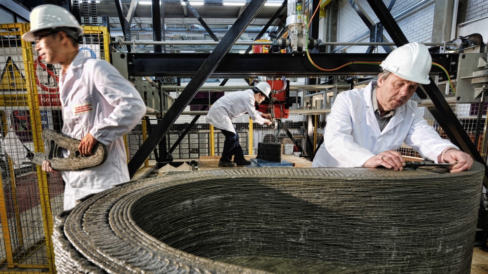 Three people working with 3D printed concrete, wearing lab coats and hard hats