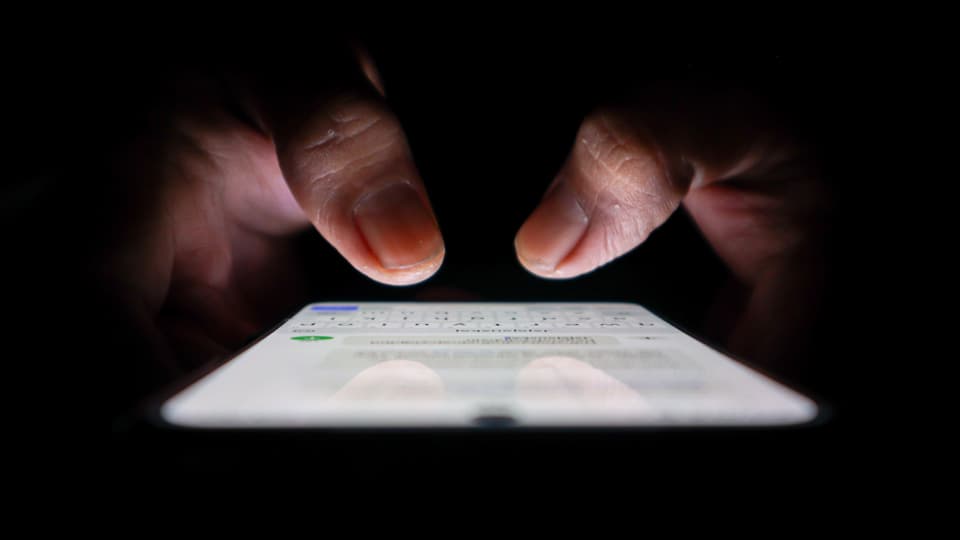 A pair of thumbs typing on a touchscreen phone with a black background.