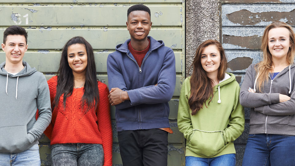 Five young people, leaning against a wall - smiling to camera