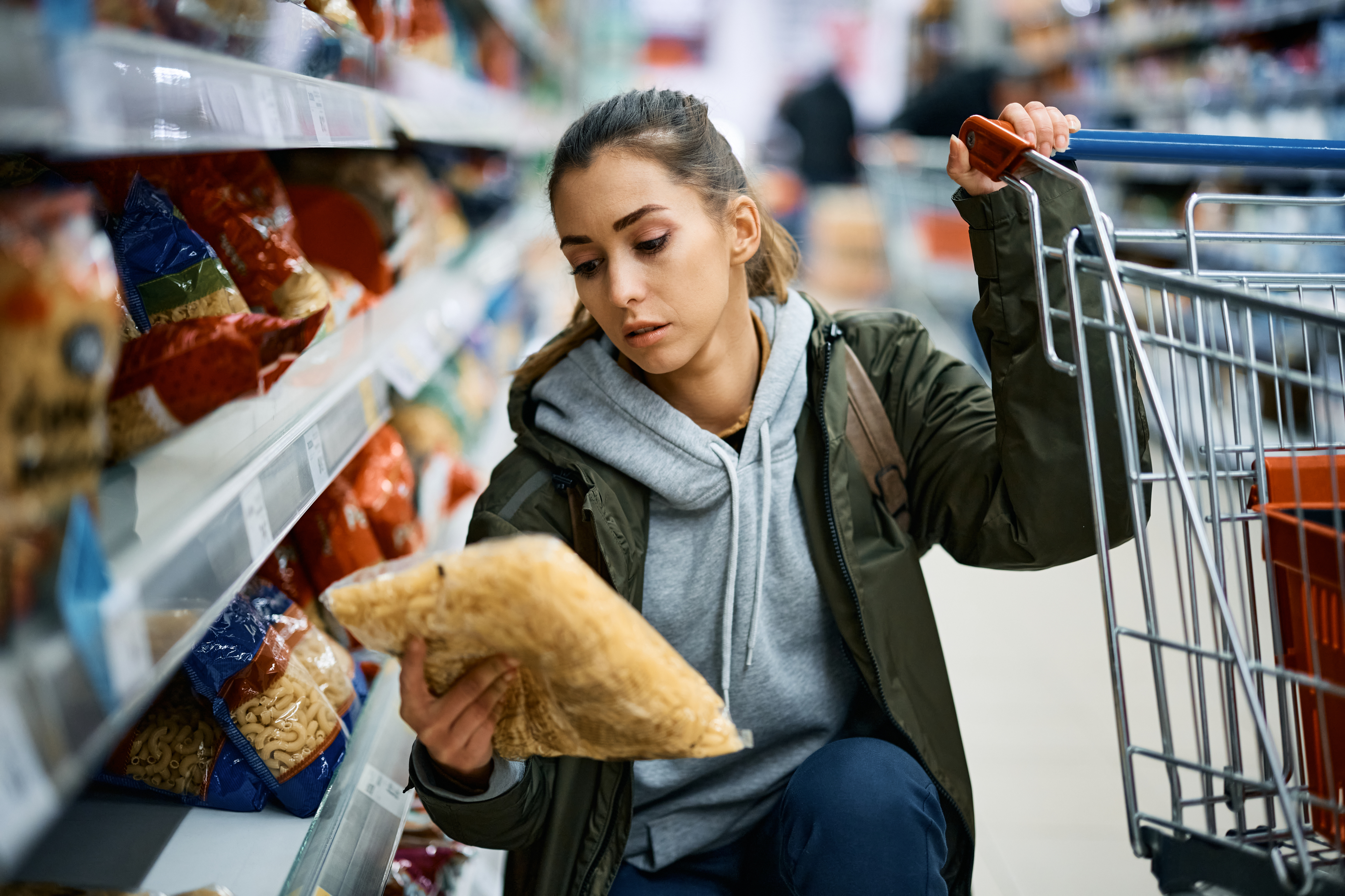 Lady holding, and looking at, a packet of pasta in the supermarket