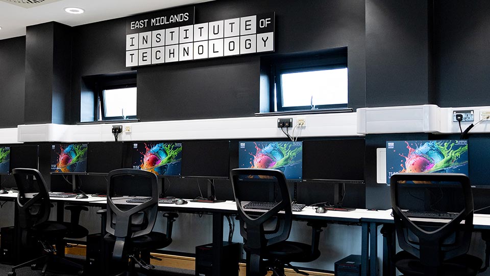 A bank of computer screens with the words 'East Midlands Institute of Technology' displayed on a wall behind