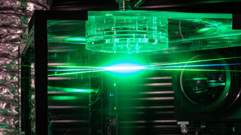 Three green laser beams converge on a central point with a clear cylinder positioned above them