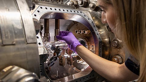 A female researcher wearing purple gloves reaching inside a metal chamber