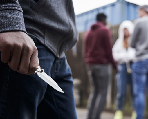 Foreground: young man holding knife. Background: a group of young people, chatting.