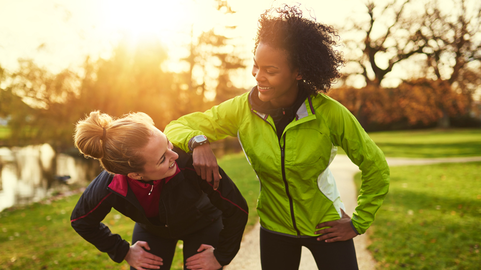 Two women laughing and recovering after a run in the park