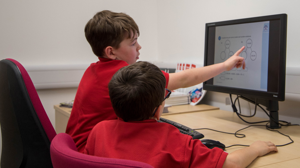 Two school pupils using a computer to work on a maths problem