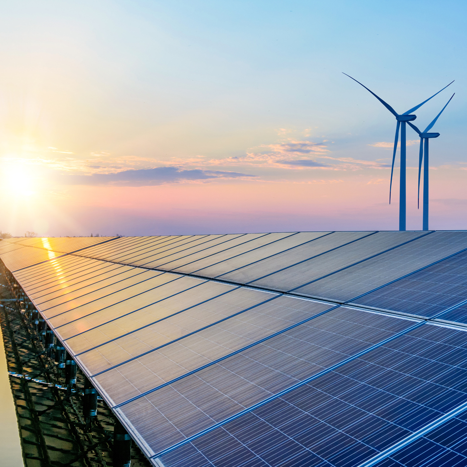 Photograph of a bank of solar panels with wind turbines in the background