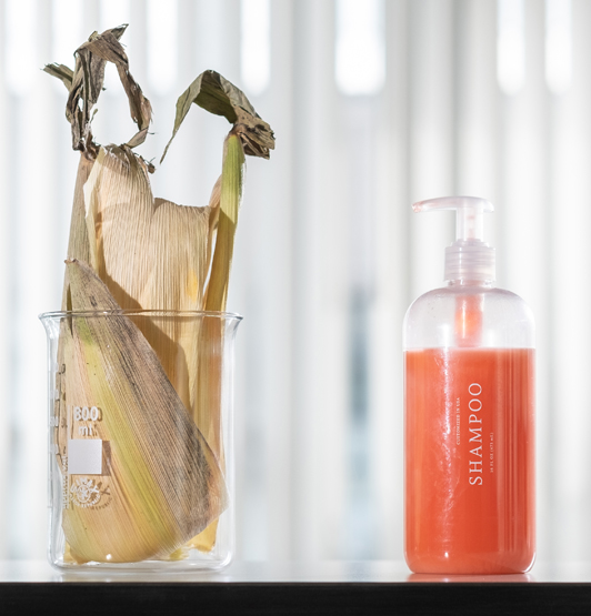 Maize husk in a beaker beside a bottle of shampoo