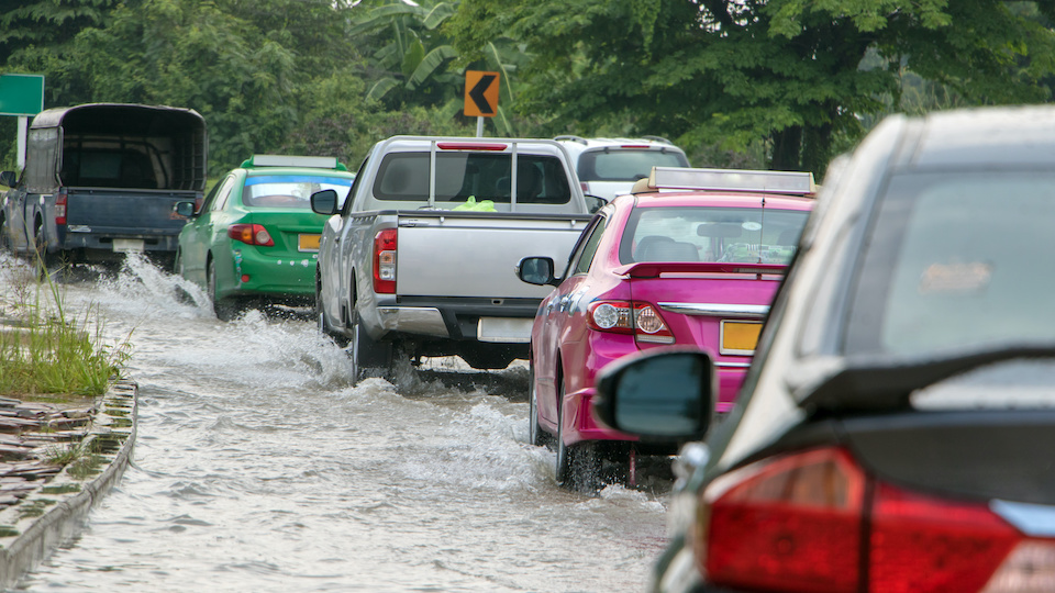 a line of cars being driven through a road that has flooded