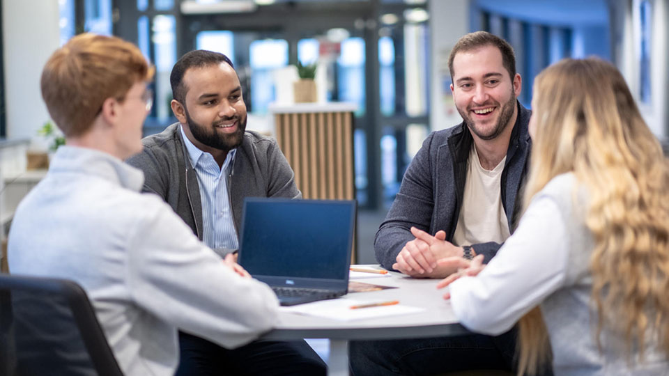 three people sitting around a table, one using a laptop