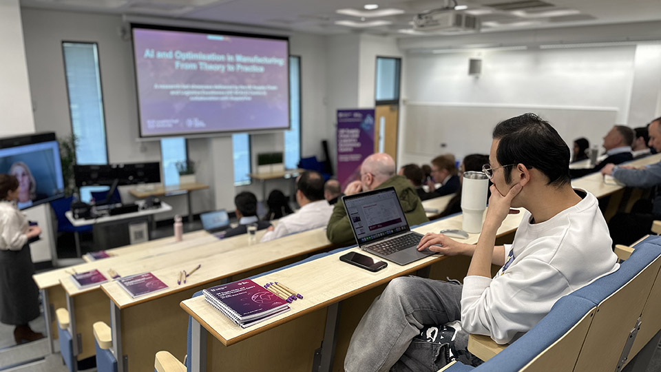 Audience attending a UK SCALE Centre event on AI and optimisation in manufacturing, with a participant taking notes on a laptop in a lecture theatre at Loughborough University.