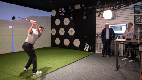 Person testing golf simulator, being monitored by an academic and the Vice-Chancellor