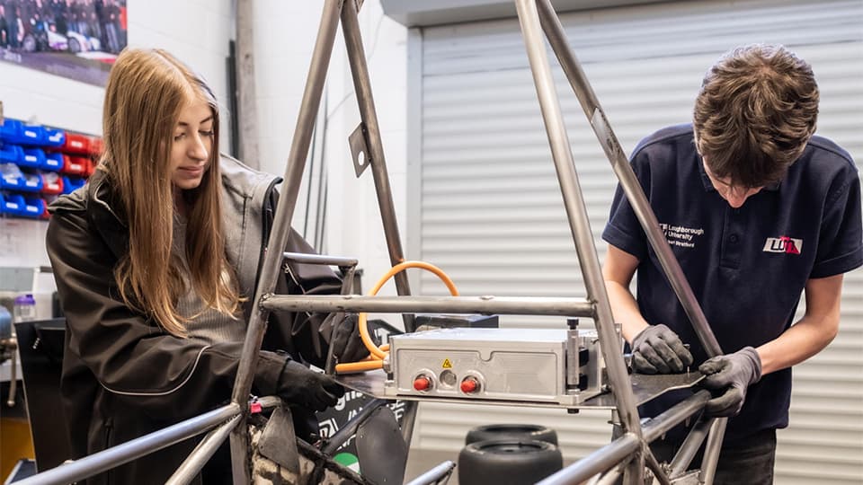 female and male student working on formula car in garage