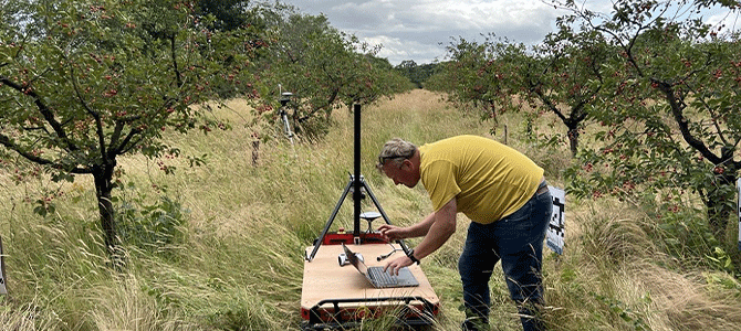 Man in field with technology scanning trees