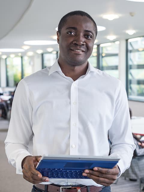 An MBA student smiling towards camera holding a laptop.