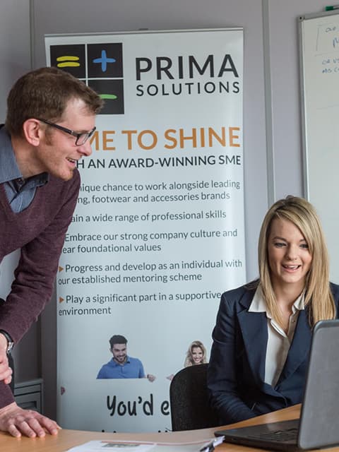 A placement student speaking with another member of staff in the office, looking at a laptop.
