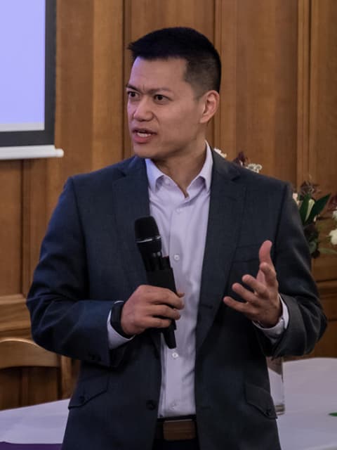 Brian Yip giving a speech. He is wearing a suit and holding a microphone.